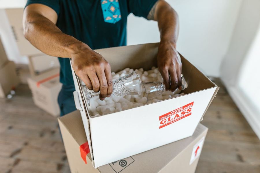 Hands carefully packing fragile glassware into a box marked handle with care